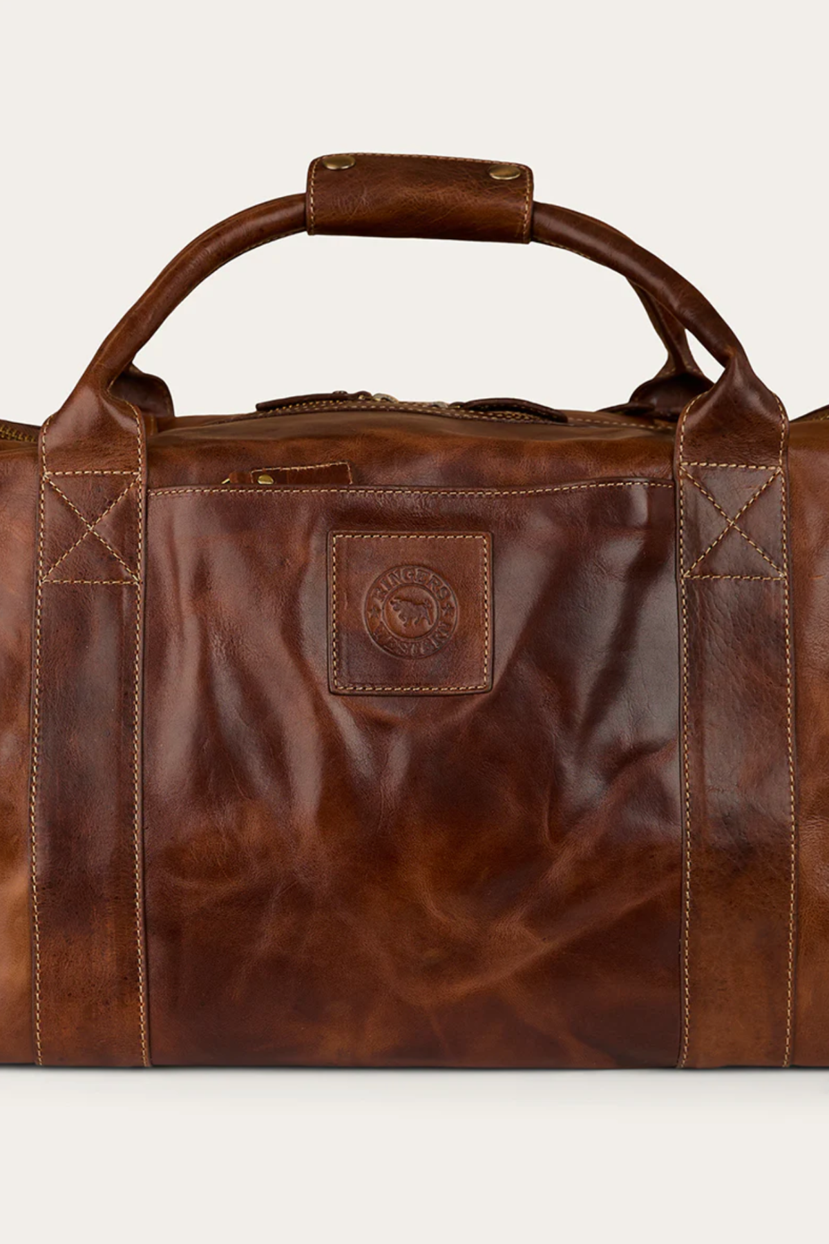 The Ringers Western Toro Gino Overniter is a brown full grain leather duffel with sturdy handles, visible stitching, and a square front patch embossed with the logoβyour ideal durable travel companion.