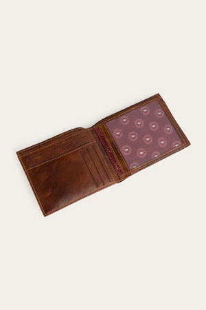 The Ringers Western Toro Grande Wallet, made from brown full grain leather, is open to display card slots on one side and a transparent compartment with a red patterned lining on the other.