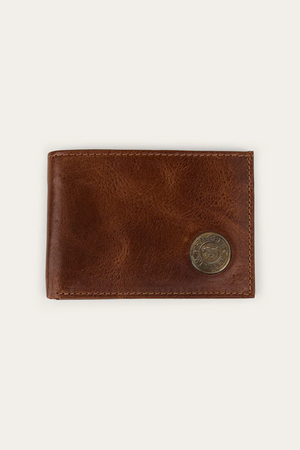 The Ringers Western Toro Slim Wallet is crafted from full grain leather with a visible texture, featuring a round metal emblem in the bottom right corner, and shown on a plain light background.