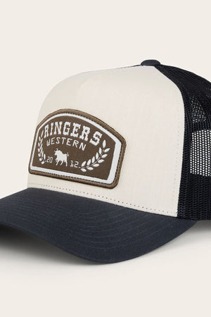The Ringers Western Wheatbelt Trucker Cap features a cream and black design with a mesh back, cotton twill front, and a patch displaying "Ringers Western," a laurel wreath, bull graphic, and "2012" on each side of the wreath.