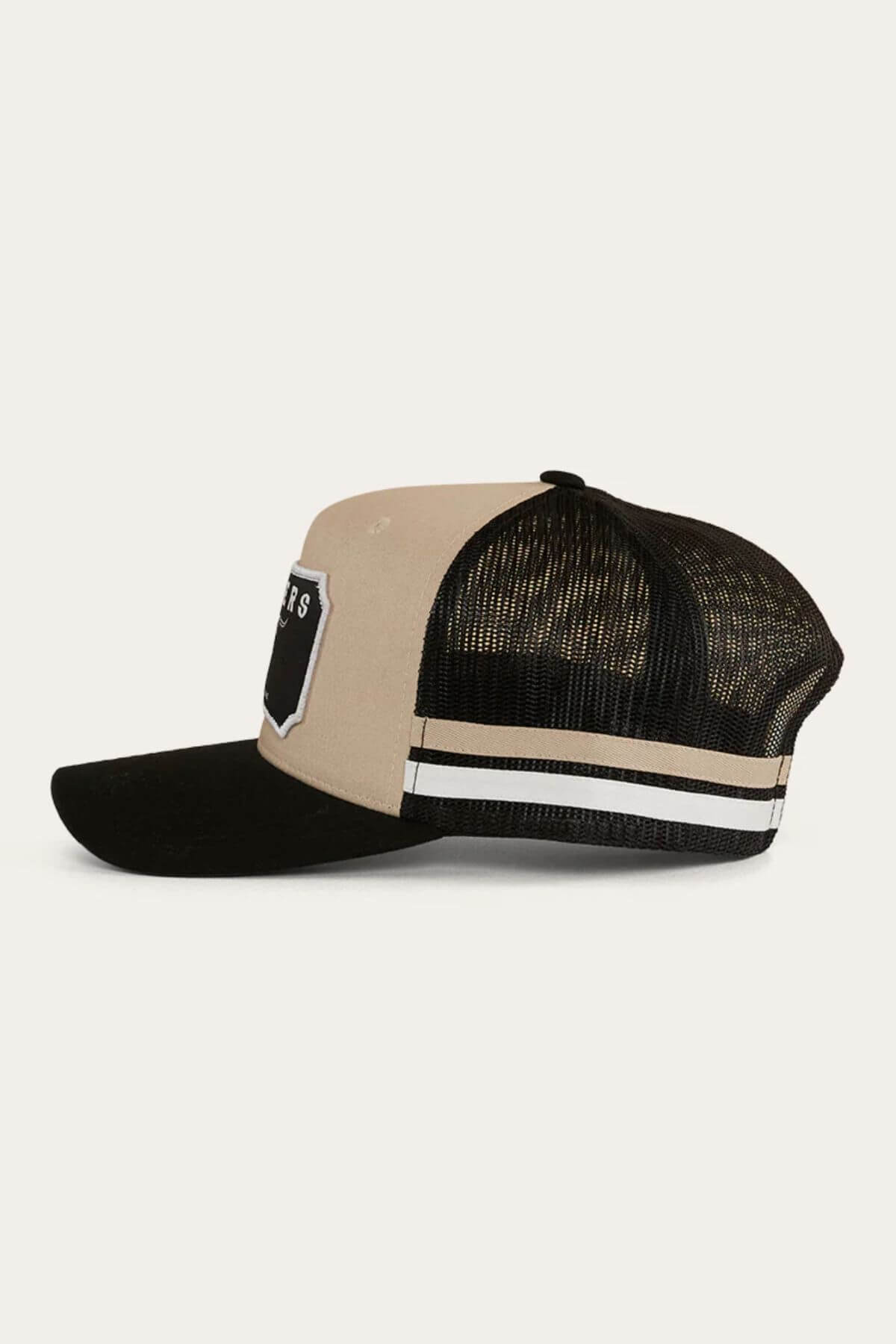 The Ringers Western Winston Trucker Cap features a beige cotton twill front, black mesh back, black curved bill, white and beige side stripes, and a bold black-and-white embroidered art patch on the front.