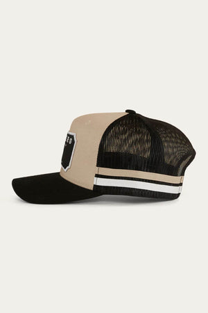 The Ringers Western Winston Trucker Cap features a beige cotton twill front, black mesh back, black curved bill, white and beige side stripes, and a bold black-and-white embroidered art patch on the front.