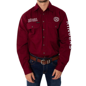A person in the Ringers Western Hawkeye Embroidered Shirt, a maroon long-sleeved work shirt with "RINGERS WESTERN" text on the chest and sleeve, stands with hands in pockets. Made from 100% cotton, it features buttoned pockets and UPF50+ protection, paired with blue jeans and a brown belt.