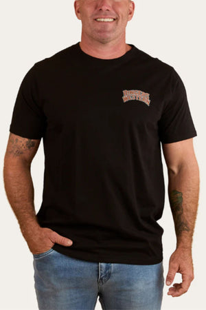 A smiling man stands with one hand in his pocket, wearing the Ringers Western Do No Harm Take No Bull Loose Fit T-Shirt in breathable black cotton jersey with a small logo on the left chest, paired with light blue jeans.
