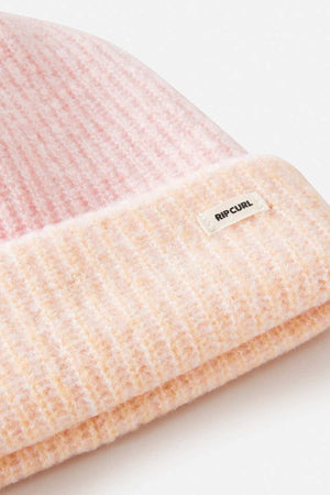 Close-up of a pink and peach Rip Curl 2 Tone Reg Revo Beanie with a small white "Rip Curl" label. This tall, ribbed beanie features a folded brim, ideal for adding style to any cold-weather outfit.