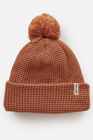 The Rip Curl Anoeta Reg Pom Pom Beanie is a cozy brown knit hat featuring a playful pom-pom, folded brim, and a small rectangular tag. Made from recycled polyester with teddy fur lining, it provides eco-friendly warmth.