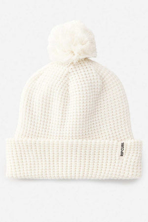 The Rip Curl Anoeta Reg Pom Pom Beanie is white with a large pom-pom, folded brim, side "RIP CURL" tag, and cozy teddy fur lining for warmth.