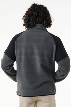 A person with curly hair is shown from the back wearing a dark gray and black Rip Curl Anti Series Archive Zip Crew and light-colored pants, standing against a plain white background.