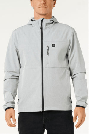 A man wears a Rip Curl Anti Series Elite Jacket in light gray—made from stretch polyester, featuring black zipper accents and a small chest pocket—standing against a plain background.