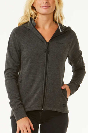 A person with long blonde hair wears a dark gray Rip Curl Anti Series Flux III Zip hooded jacket, featuring bonded polar fleece, long sleeves, and a subtle logo on the upper left side, with their left hand in the pocket.
