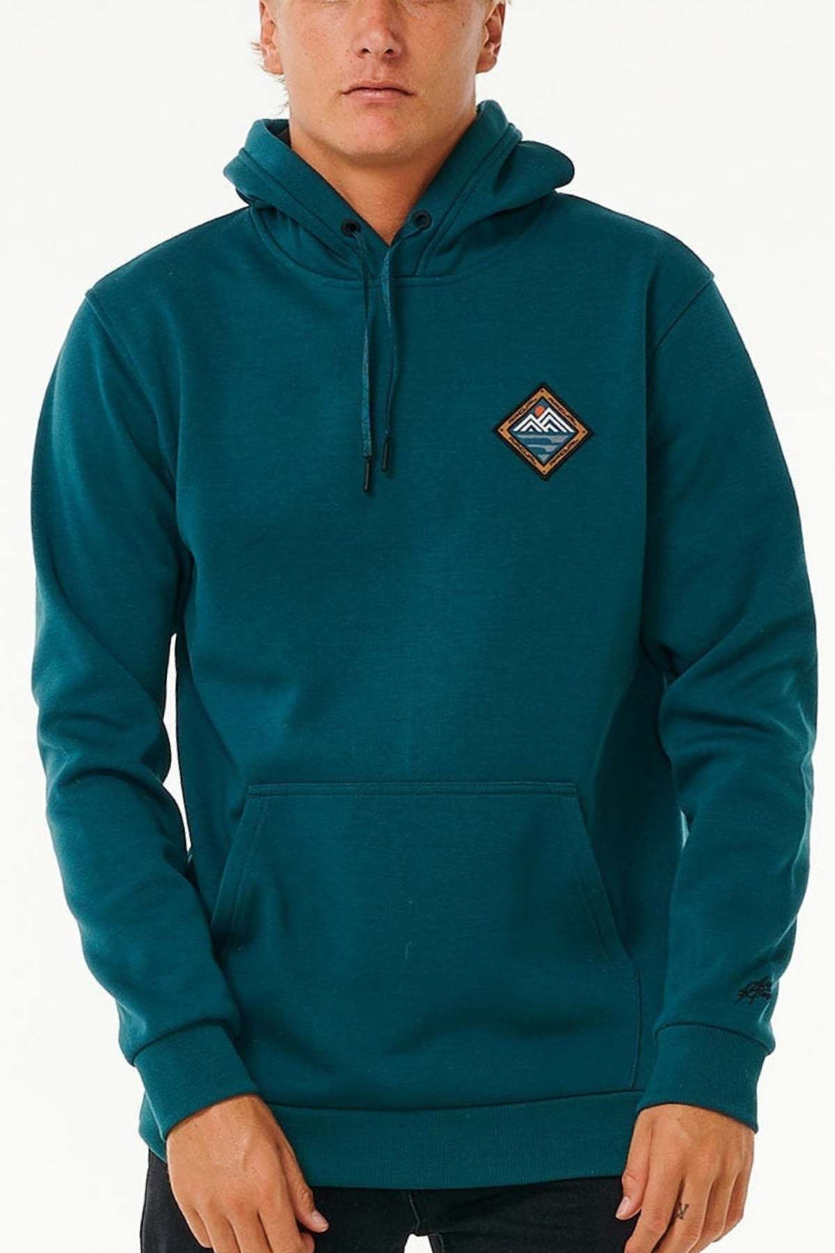 A person in a teal Rip Curl Anti Series Journey Hood with thumb holes, a front pocket, and a triangular mountain patch on the chest. It features water-repellent fabric and drawstrings, with their hands partially tucked into the cozy pocket.