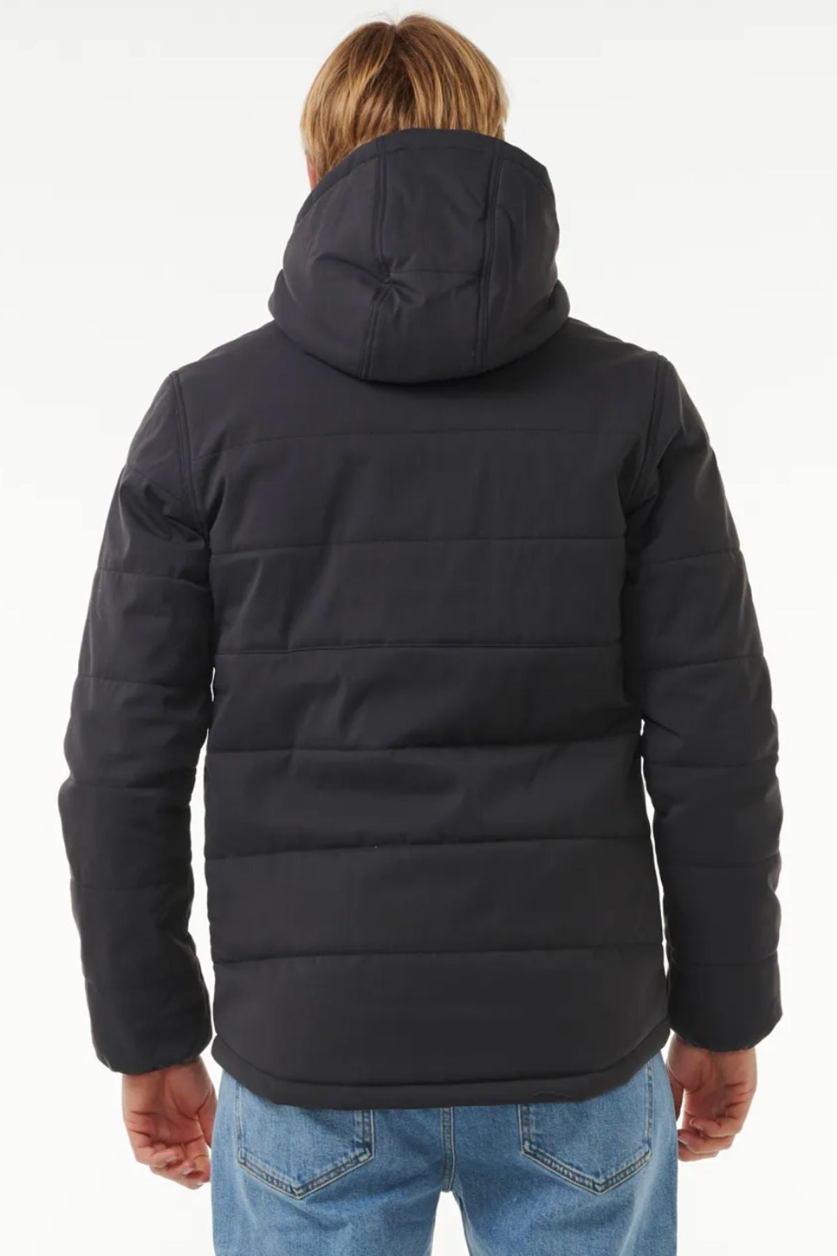 A person with blonde hair is seen from behind, wearing the Rip Curl Anti Series Ridge Jacket with quilted lining and blue jeans, set against a plain white background.