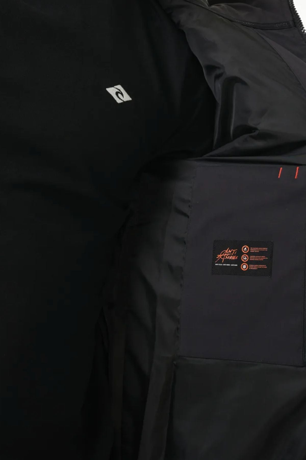 Close-up view of the inside lining of a black Rip Curl Anti Series Ridge Jacket, featuring a small stitched label with text and symbols, alongside a partial logo visible on an adjacent black shirt.