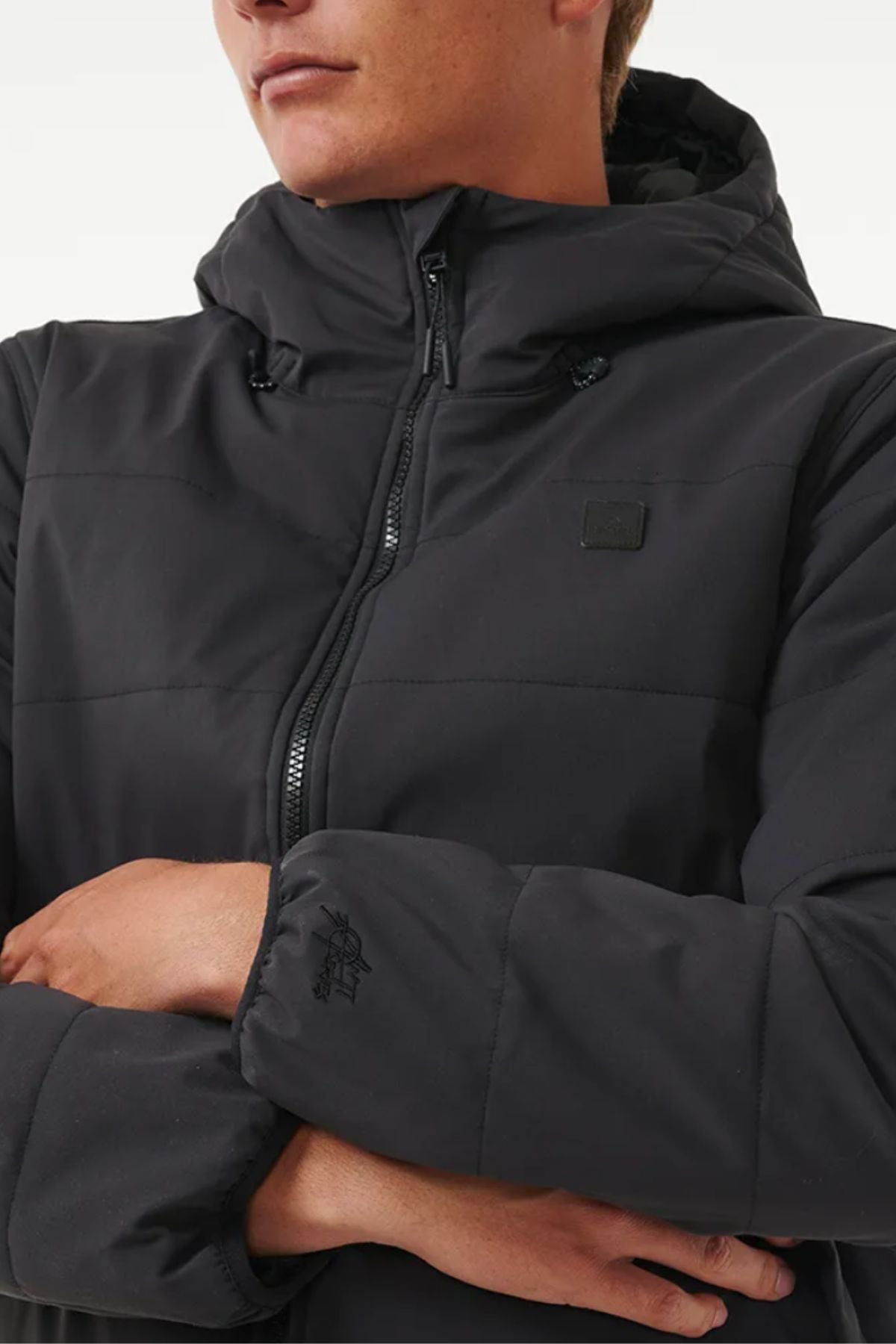 Wearing a black Rip Curl Anti Series Ridge Jacket with quilted padded lining and a front zipper, arms crossed and partial face visible.