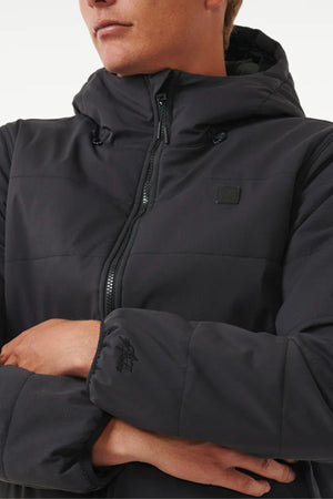 Wearing a black Rip Curl Anti Series Ridge Jacket with quilted padded lining and a front zipper, arms crossed and partial face visible.