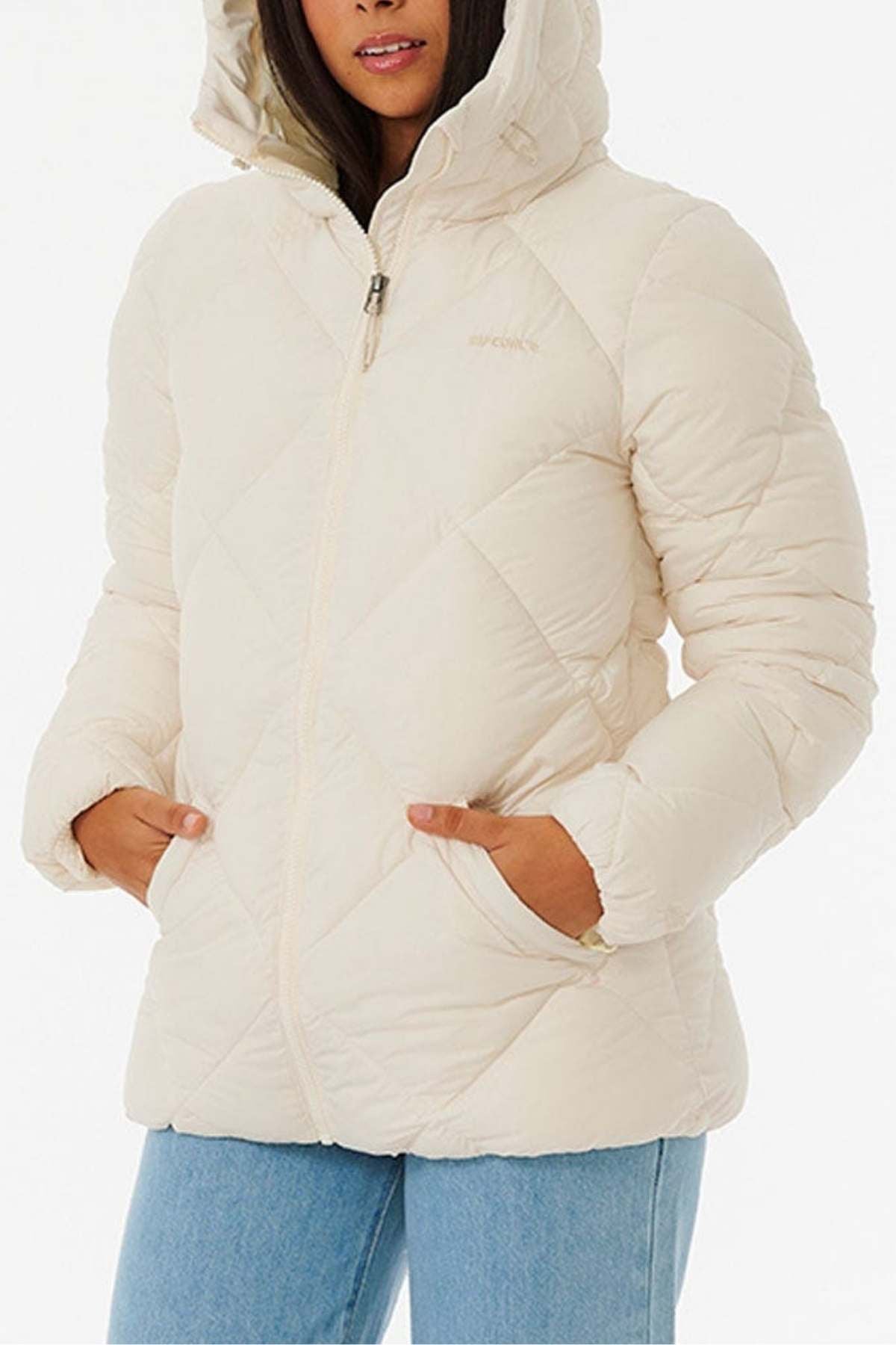 Wearing a quilted cream Rip Curl Anti Series Shorebreak Jacket with a hood and front zipper, hands in pockets, paired with light blue jeans against a plain white background.