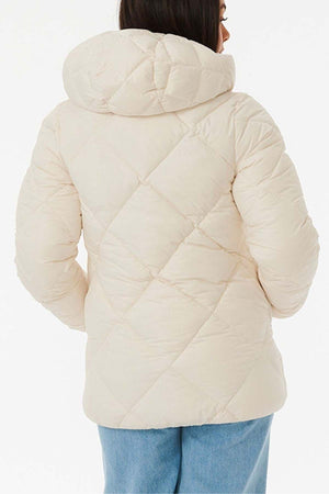 A person in a Rip Curl Anti Series Shorebreak Jacket, a cream-colored, water-repellent quilted puffer with a hood, stands with their back to the camera. Paired with blue jeans on a white background, it blends style and functionality for light shower resistance.