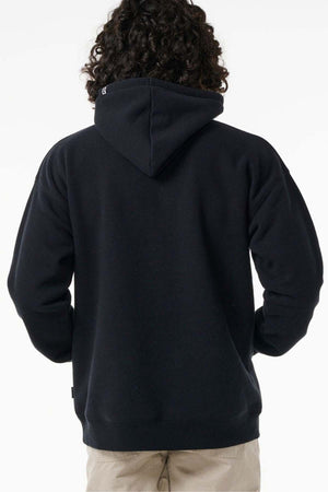 A person with curly hair is shown from the back, wearing a black Rip Curl Archive Ocean Tech Hood sweatshirt and beige pants, highlighting surf-inspired style against a plain white background.