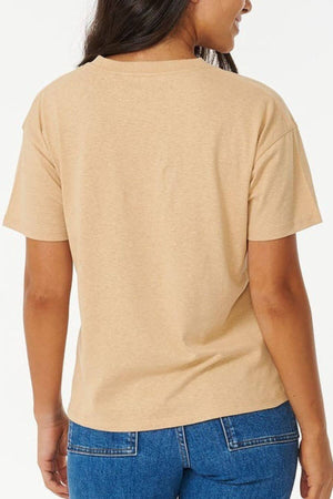 A person with long dark hair is seen from behind in a Rip Curl Balance Relaxed Tee with a playful front print and blue jeans against a plain white background.