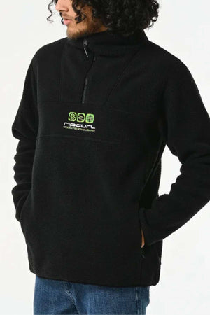 Man wearing Rip Curl Bells Polar Fleece in black with a 1/4 zip and green and white logo on the chest, paired with blue jeans.