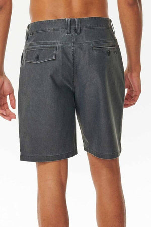 A person stands with their back to the camera, highlighting Rip Curl Boardwalk Epic Mix shorts in dark gray. These shorts feature belt loops, multiple pockets, and a vintage-inspired look. Made from quick-dry fabric, they're perfect for adventures against the plain light background.