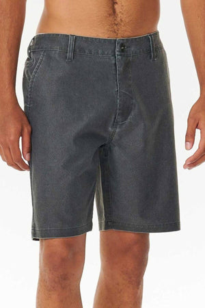 A person wears Rip Curl Boardwalk Epic Mix shorts featuring a vintage-inspired style. These mid-thigh denim shorts, with front button and zipper closure, are showcased against a plain backdrop that highlights their timeless charm.