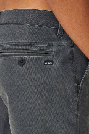 Close-up of a person wearing Rip Curl Boardwalk Epic Mix pants in dark green corduroy, highlighting the side and back pockets with a vintage vibe. A small black "Rip Curl" label is sewn near the waistband.