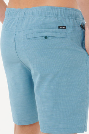 Close-up of a person wearing Rip Curl Boardwalk Jackson Volley shorts, highlighting the buttoned back pocket, small brand label near the waistband, and one hand partially tucked into a side pocket.