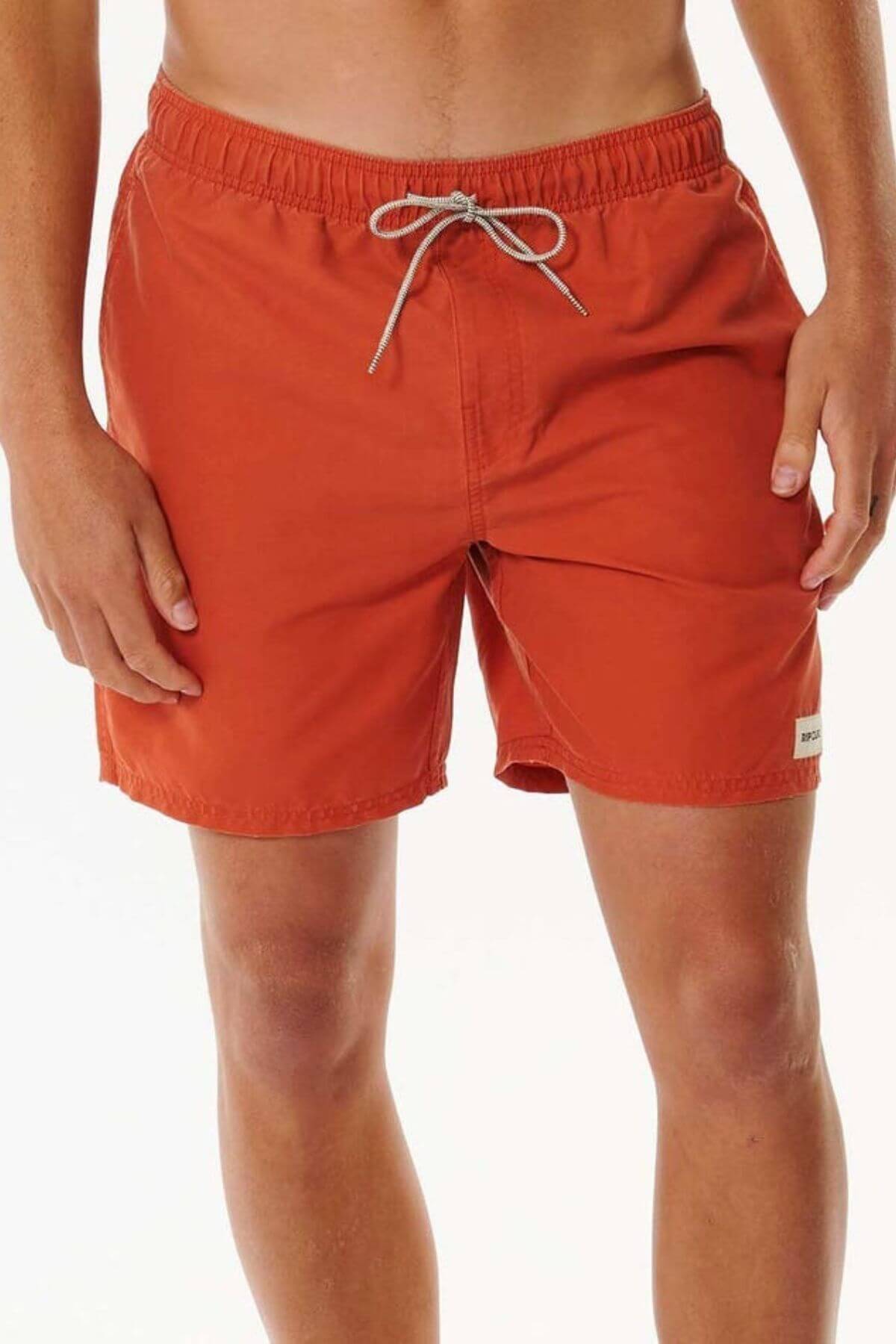 Against a white background, someone wears vibrant orange Rip Curl Bondi Volley board shorts featuring a white drawstring and a label on the left leg. Made from recycled PET, their arms are relaxed by their sides.