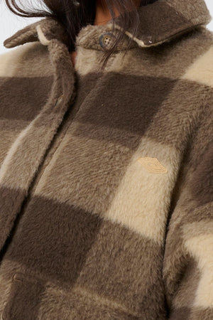 A close-up of a person wearing the Rip Curl Cala Nights Check Jacket, featuring fuzzy brown and beige plaid, a buttoned collar, and a small embroidered chest patch.