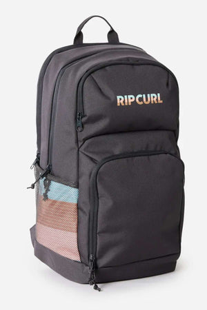 The Rip Curl Chaser 33L Backpack is black, made from recycled polyester, with multiple zip compartments, a 15" laptop sleeve, front pocket, mesh side pocket, top handle, and "RIP CURL" in gradient colors on the front.
