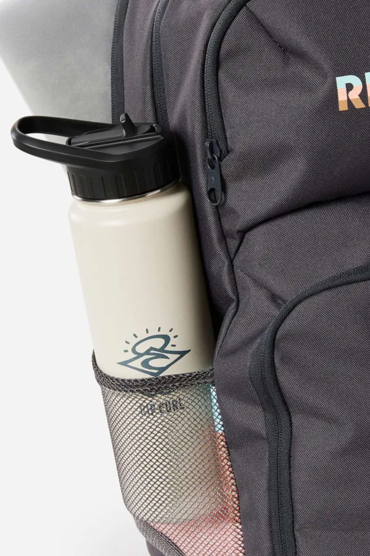 A light-colored water bottle with a black lid and "RUN" graphic sits in the mesh side pocket of a dark gray Rip Curl Chaser 33L Backpack, made from recycled polyester and compatible with 15" computers.
