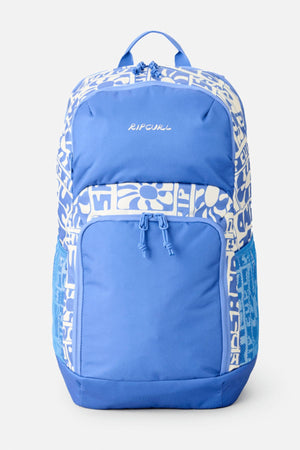 The Rip Curl Chaser 33L Backpack features a blue color with white abstract pattern, front zip pocket, side mesh pockets, and top handle. Made from recycled polyester, it offers eco-friendly style and practical organization.