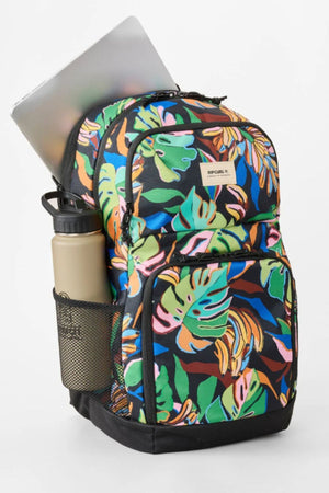 The Rip Curl Chaser 33L Backpack, featuring a tropical leaf print and crafted from recycled polyester, holds a silver laptop in its main compartment and a beige water bottle in the black mesh side pocket, all set on a white background.