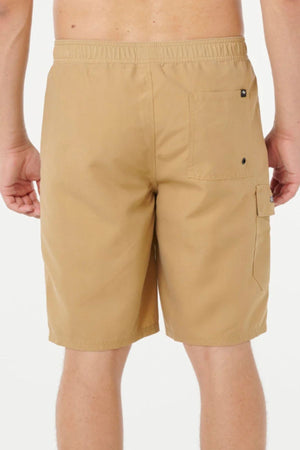 A person is shown from the waist down, wearing tan Rip Curl Classic Surf Cargo Shorts with an elastic waistband, right back pocket, and side flap pocket, standing against a plain white background.