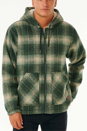 Someone stands against a plain light background wearing the Rip Curl Classic Surf Check Jacket, a green and white polyester plaid zip-up with front pockets and a sherpa-lined hood.