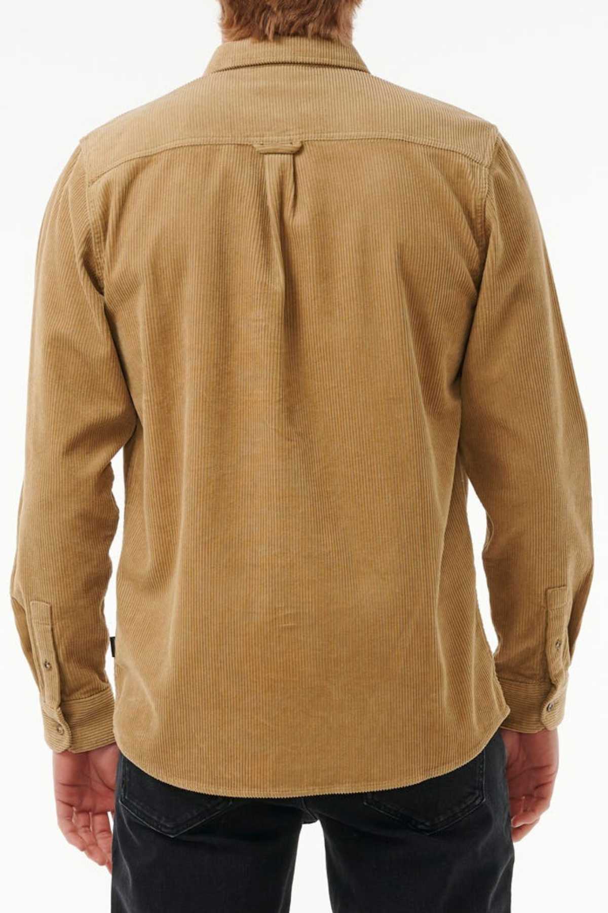 A person with light hair wears the Rip Curl Classic Surf Cord Shirt, showcasing a stylish and functional light brown corduroy design with long sleeves, a back yoke, and pleat detail. They pair it with black pants against a plain white background.