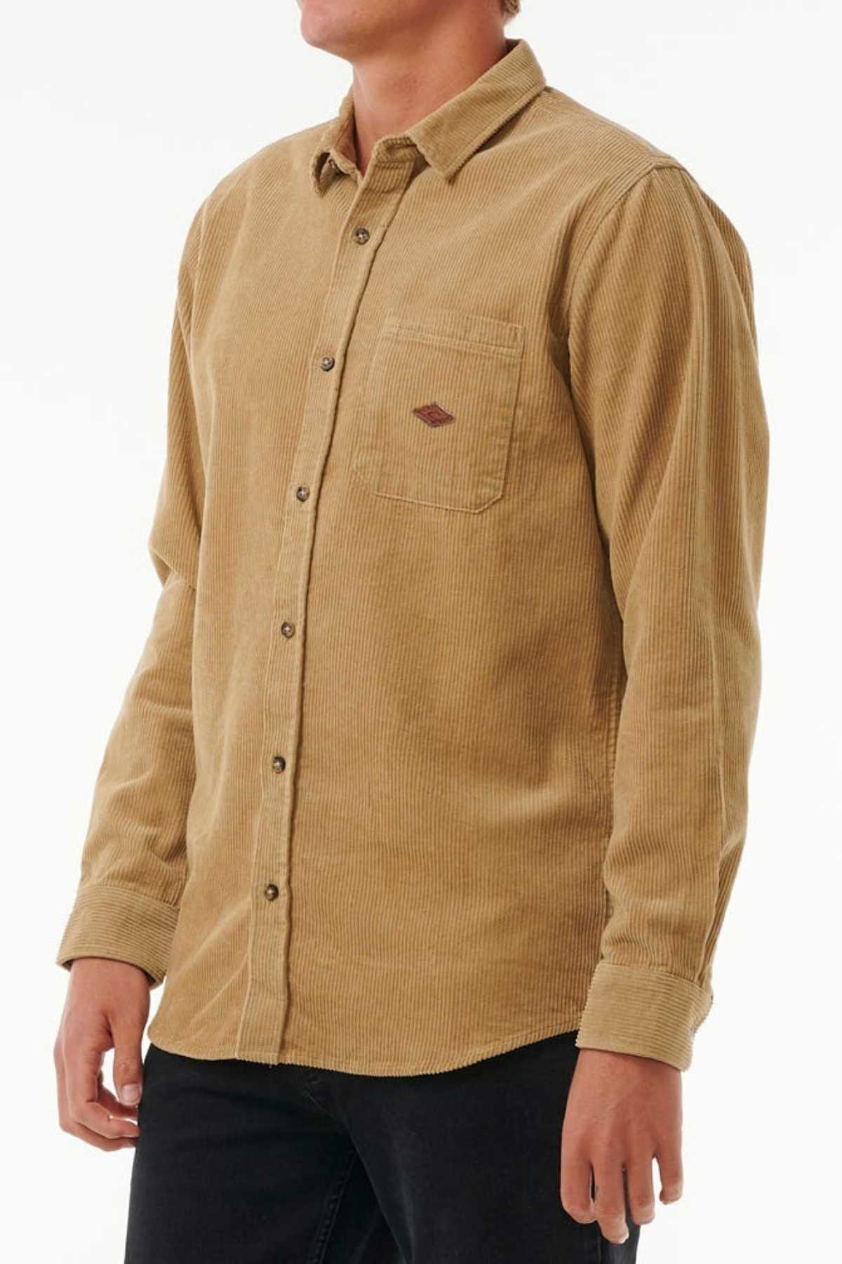 A person wears a Rip Curl Classic Surf Cord Shirt crafted from 300G cotton corduroy, featuring a chest pocket with an embroidered logo, paired with black pants against a white background.