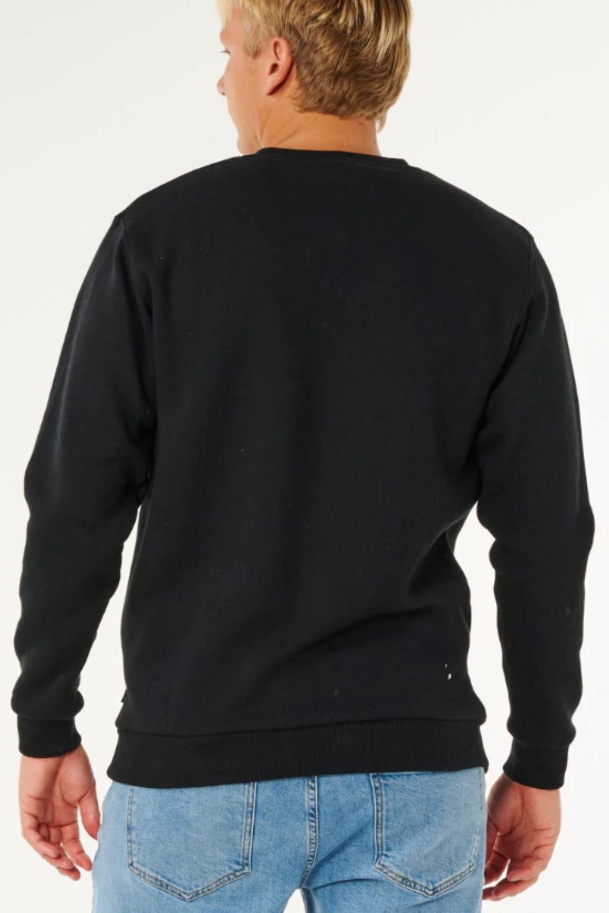 A person with short blond hair is shown from the back, wearing a plain black Rip Curl Classic Surf Crew sweatshirt and light blue jeans against a plain, light background.