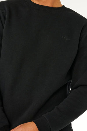 A person wears a plain black Rip Curl Classic Surf Crew sweatshirt, shown from shoulders to hips with one hand near the bottom against a light background—an ideal essential for any casual surf-inspired look.