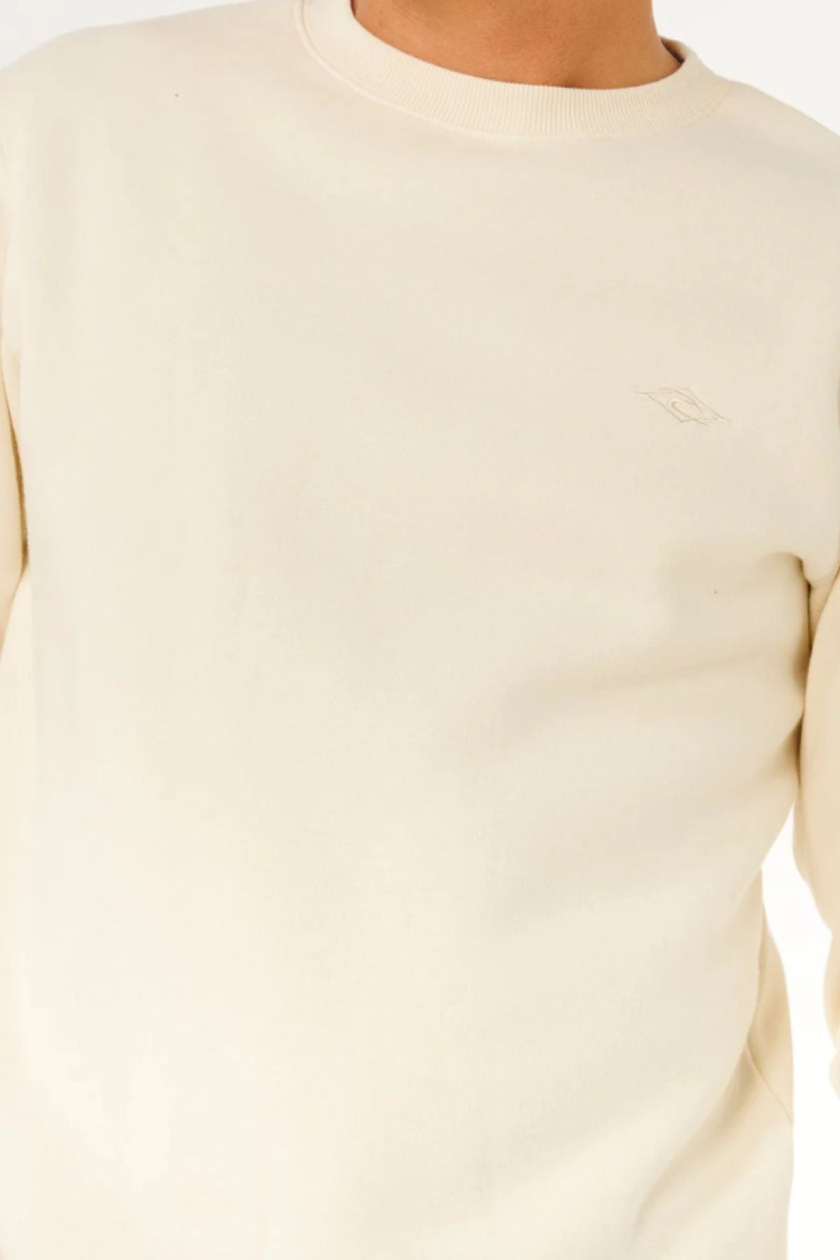 A person wearing a cream Rip Curl Classic Surf Crew sweatshirt with subtle stitching and an embroidered logo on the chest, shown from shoulders to waist against a plain background.