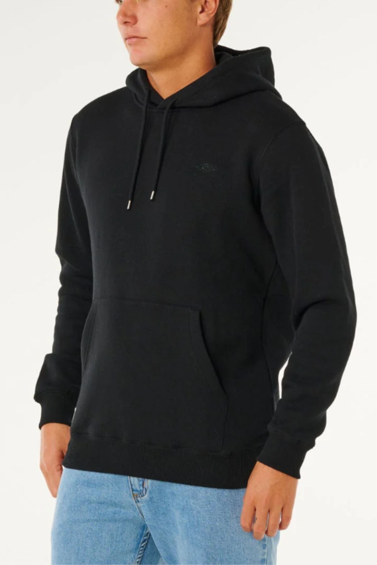 Someone in the Rip Curl Classic Surf Hood in plain black, featuring a front pocket, paired with light blue jeans, stands against a light background.