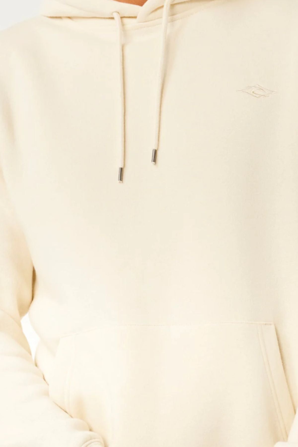 Close-up of a person wearing the Rip Curl Classic Surf Hood in light beige with a front pocket and drawstrings. Only the lower face, chest, and arms are visible.