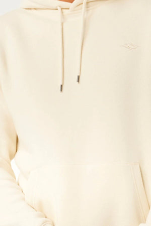 Close-up of a person wearing the Rip Curl Classic Surf Hood in light beige with a front pocket and drawstrings. Only the lower face, chest, and arms are visible.