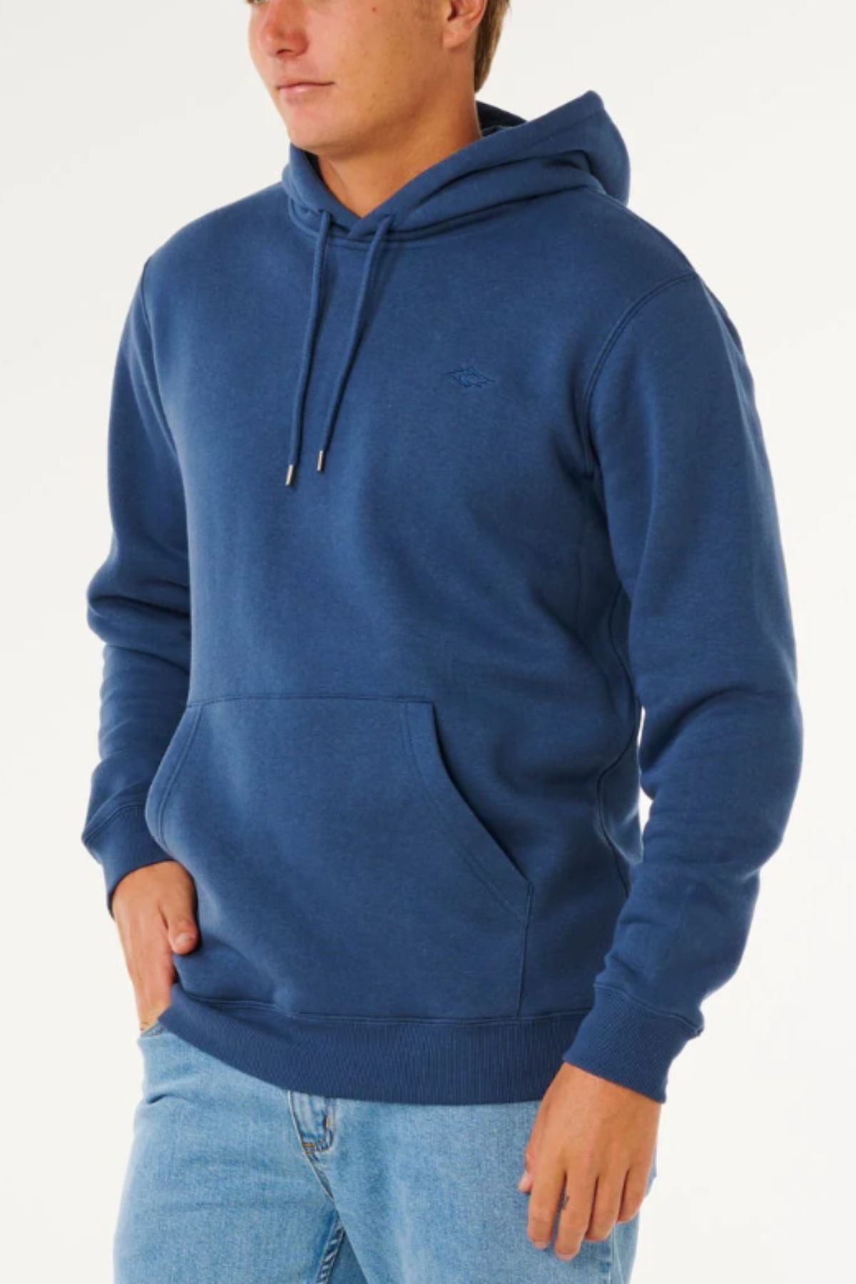 A person wears the Rip Curl Classic Surf Hood in blue, featuring a front pocket and drawstrings, paired with light blue jeans, standing against a plain white background.