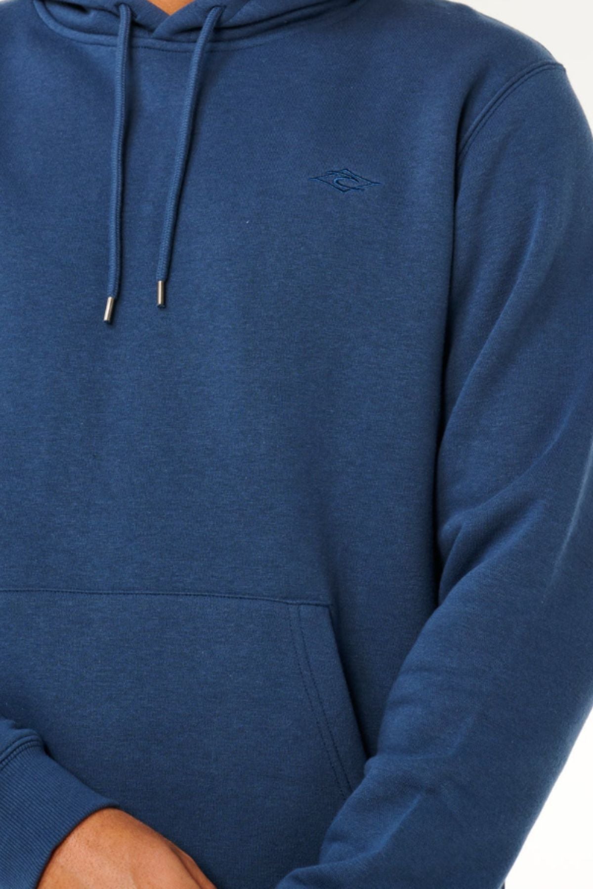 A person wearing a blue Rip Curl Classic Surf Hood with a small embroidered logo on the chest stands with arms crossed, showing only their torso and part of their arms.