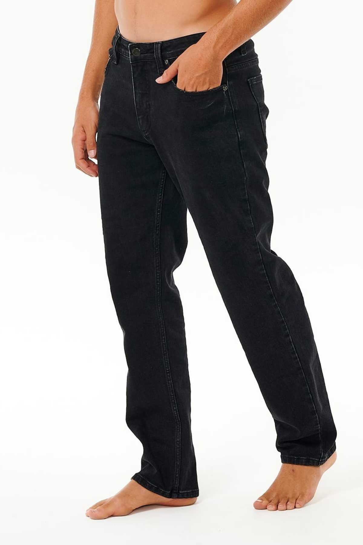 A person, barefoot and shirtless, stands against a plain white background wearing Rip Curl Classic Surf Jean—straight-leg jeans made from stretch cotton denim with classic five-pocket styling and one hand near the waistband.