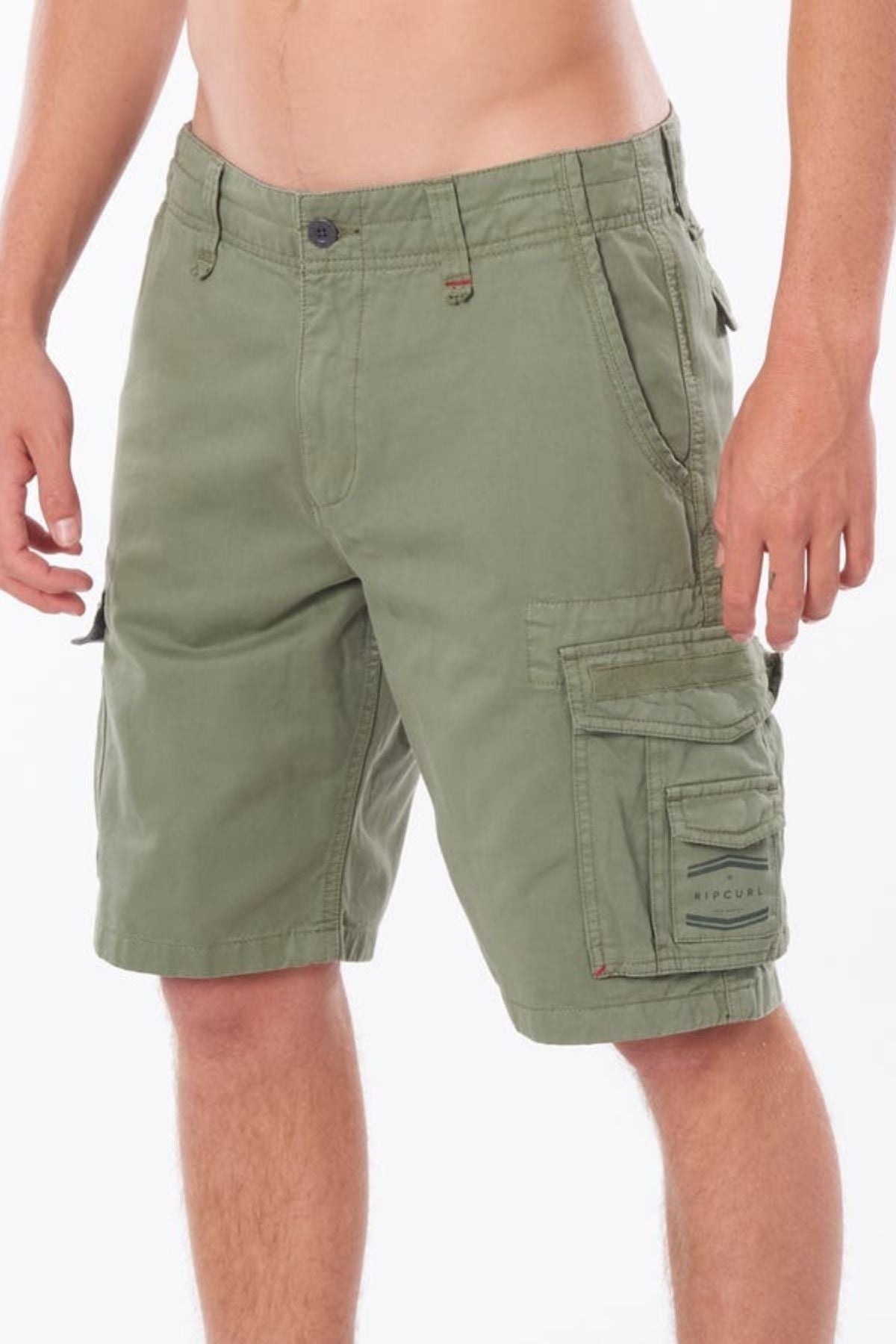 A person wearing the Rip Curl Classic Surf Trail Cargo Short, made of 100% cotton in olive green, is shown from the waist down. The distinctive look includes multiple pockets and a button closure, all set against a plain white background.