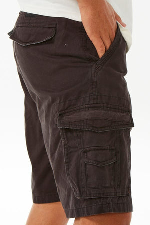 A person is standing against a plain white background, wearing dark brown Rip Curl Classic Surf Trail Cargo Shorts with multiple pockets. One hand, partially visible, is resting in the side pocket. The view captures the right side of the relaxed fit shorts and part of a white shirt.