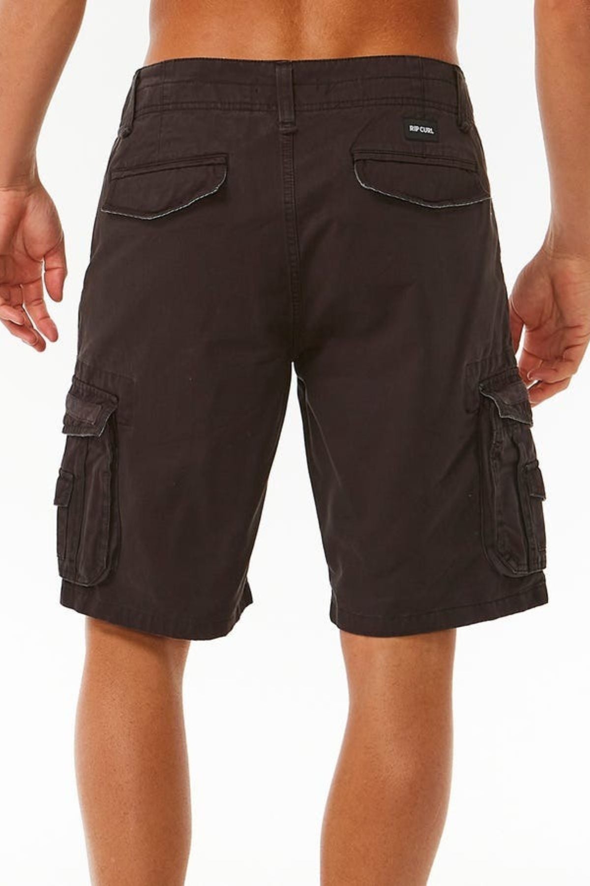 A person wearing the Rip Curl Classic Surf Trail Cargo Short is standing with their back to the camera. The dark brown, relaxed-fit shorts feature multiple pockets, including two back flap pockets and two side cargo pockets with flap closures. The person has a tan complexion and is shirtless.